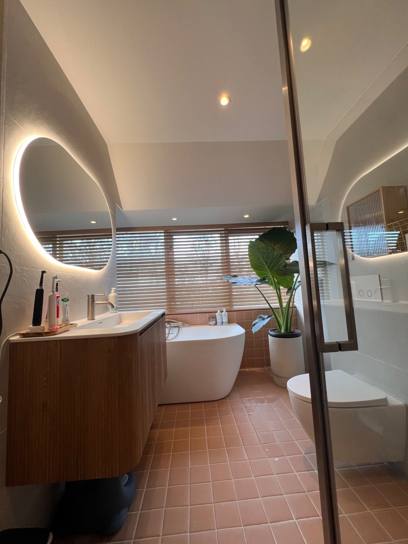 Gerenoveerde badkamer met houten wastafelmeubel en ronde verlichte spiegel
